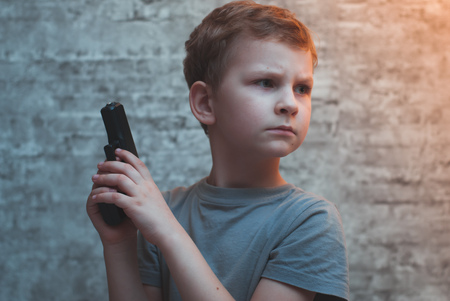 Boy with a gun in his hand against the brick walls, dramatic portraitの写真素材