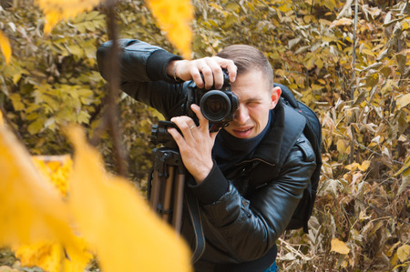 Photographer in a leather jacket shoots in autumn Park, professional person during a photo shoot outdoorsの写真素材