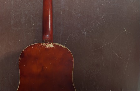 Old acoustic guitar leaning on grungy wooden wall, guitar in poor condition, the background musicの写真素材