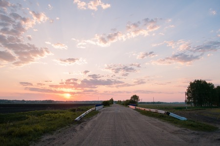 Dawn on a rural road, green meadow, bridge on the roadの写真素材