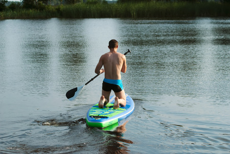 A man floats on a sup Board on the lake, rear view, paddle on the Board, forest lakeの写真素材