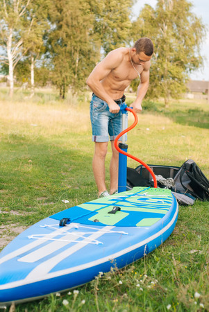 Guy inflates SUP Board with pump, sporty young man, paddle boardingの写真素材