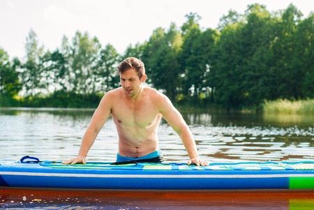 The guy is engaged in paddle boarding on the lake, the man on the SUP Board, vertical photoの写真素材
