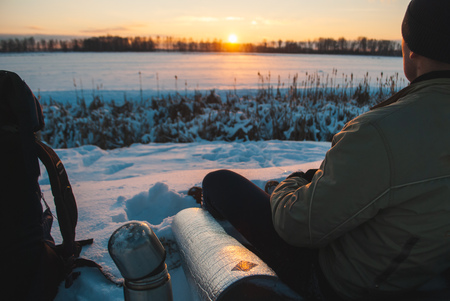 Man watching the sunset in the winter evening, winter tourism, camping in the snow close-upの写真素材