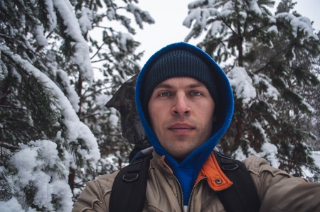 a man in a blue hood takes a selfie in the winter forest on the background of snow-covered trees, a walk in the winter forest, unity with nature,の写真素材