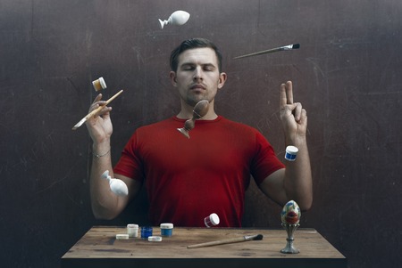 the Creator makes objects fly, the concept of preparation for Easter, a set of wooden homemade eggs, paint and brushes, a creative person in a red t-shirtの写真素材