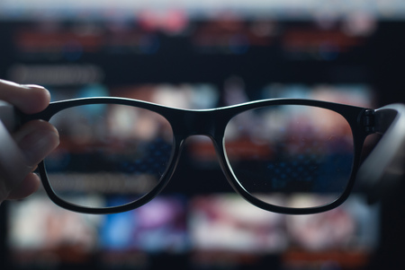 hand holding black glasses on the background of the monitor, vision deteriorated due to the long stay at the computer, poor vision and glasses do not helpの写真素材