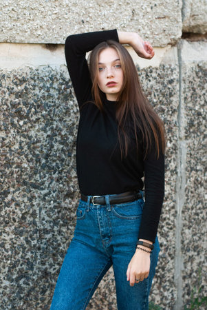 Beautiful slender girl in blue jeans posing at the concrete wall,