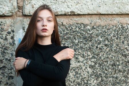 Beautiful young girl in a black turtleneck sweater posing in the concrete wallの写真素材