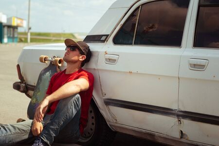 Young skater in the red shirt resting at the old cars, the journey to longboneの写真素材