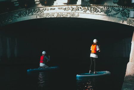 Girls float paddle Board under the bridge, women in safety helmet, photo in low key,の写真素材