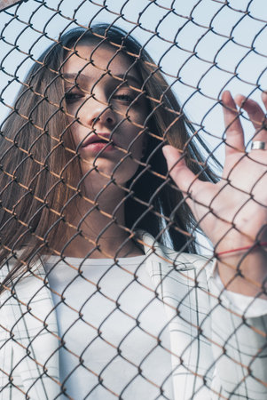 Girl holding hand on metal chain wire mesh, concept of abuse of women human trafficking, crime and...