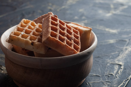 Delicious waffles in a wooden bowl, on a black background.