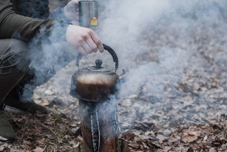 A tourist makes tea in the forest, an old teapot on a fireの写真素材