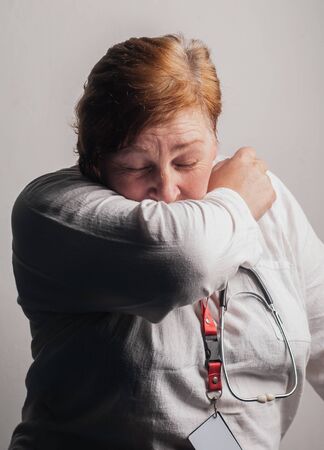 A woman sneezes in her elbow, medical staff are illの写真素材