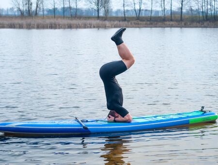 SUP YOGA, a man in a wetsuit doing yoga on a cloudy day, headstand on a paddle Boardの写真素材