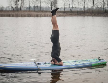 SUP YOGA, a man in a wetsuit doing yoga on a cloudy day, headstand on a paddle Boardの写真素材