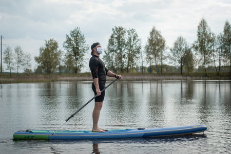 sports man in a medical mask rowing a paddle standing on a Board, prevention of covid,