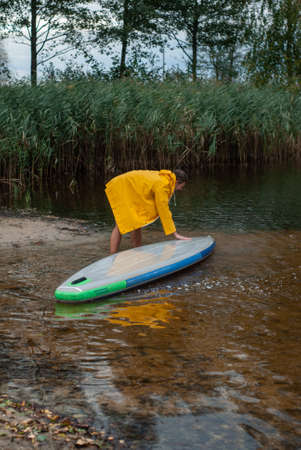 A man in a yellow raincoat washes an inflatable Board,,の写真素材