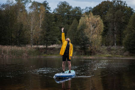 A man in a yellow raincoat throws an oar while standing on a paddleboard,の写真素材