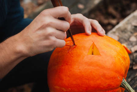 guy carves Jack o lantern out of pumpkin close up,の写真素材
