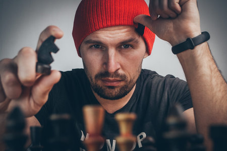 a chess player in a red cap moves a black knight driving the white king into a corner