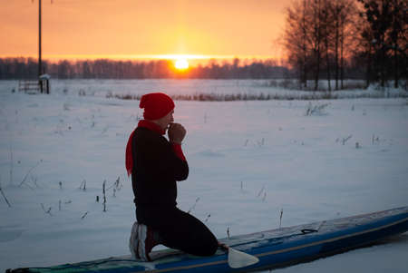 a sporty man in a red hat with a paddle stands on an inflatable board in the middle of the snow, winter sup boardの写真素材