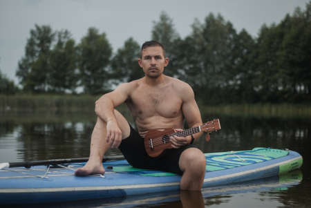 a man with a ukulele sits on a surfboardの写真素材