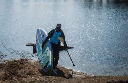 paddle board traveler, a man in a dry wetsuit goes to the waterの写真素材