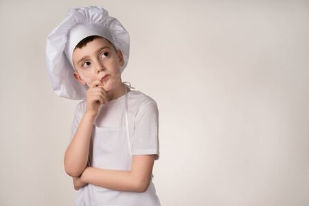 A cute little boy in a chefs costume cooks food with emotions thinksの写真素材