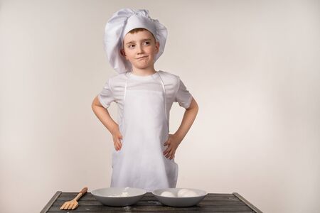 A cute little boy in a chefs costume cooks food with emotions thinksの写真素材