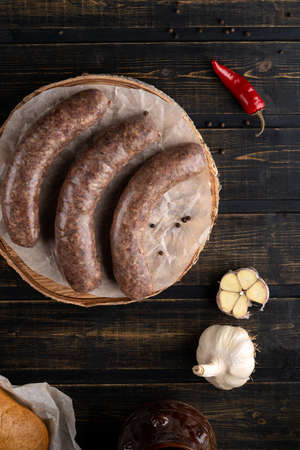 raw sausages in the skin composition top and side view with vegetables and herbs on a dark treeの写真素材