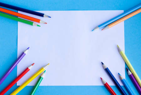 Multi-colored pencils and a white sheet of paper on a blue background. The concept of creativity, development, learningの写真素材