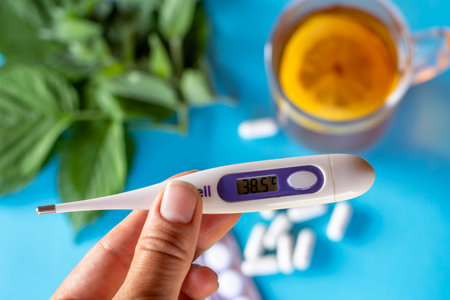 A thermometer showing a temperature of 38.5 degrees in the hand against the background of tea with...