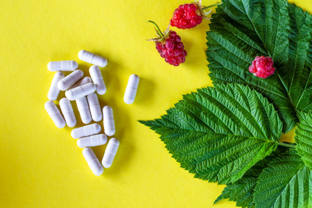 Pills (drugs), raspberry leaves and berries on a yellow background. The concept of treatment of...
