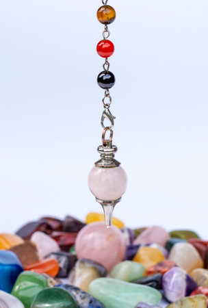 Pendulum made of natural stones (rose quartz) against the background of semi-precious multi-colored stones.の写真素材