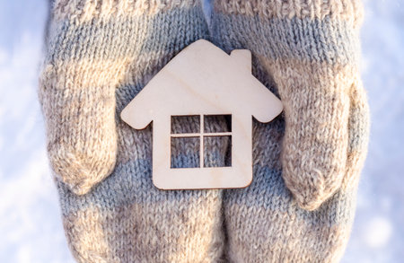 Hands in knitted mittens hold a wooden house close-up. Warm home, winter holidaysの写真素材