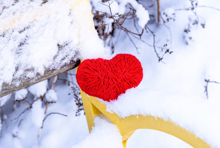 A red heart is a symbol of love lying on a snow-covered benchの写真素材