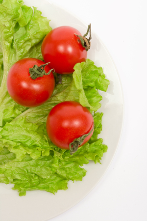 Three cherry tomatoes, lettuce leaves on a white plate and white backgroundの写真素材