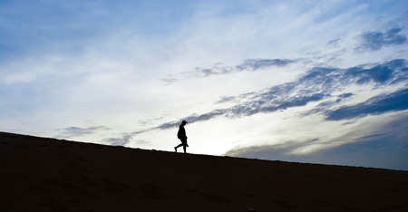 Silhouette man walking down desert  with clouds blue sky background in the morningの写真素材