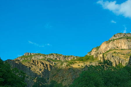 Rocky and forested mountains near Geghard monastery, on a sunny and cloudy day, at sunset, during golden hourの写真素材