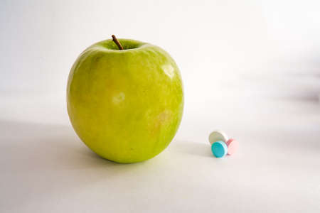 Green apple or vitamin pills on a white background. Healthy eating, diet, lifestyle concept, treatment choice conceptの写真素材