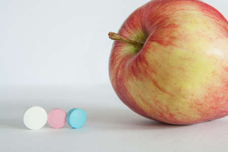 Red apple or vitamin pills on a light gray background. Healthy eating, diet, lifestyle concept, treatment choice concept. High-quality photoの写真素材