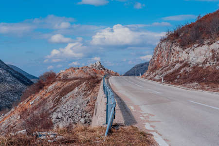 The Asphalt road in the mountains. Landscape view perspective of mountain road with white clouds on blue sky. Traveling by car. Design element of roadの写真素材