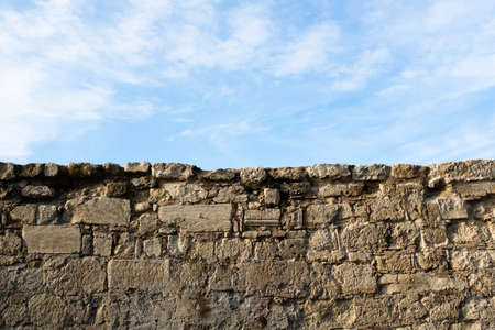 Stone wall and blue sky with white clouds. Landscape background from brick wall and sky for poster, branding, calendar, multicolor card, banner, cover, post, header for website. High quality photoの写真素材