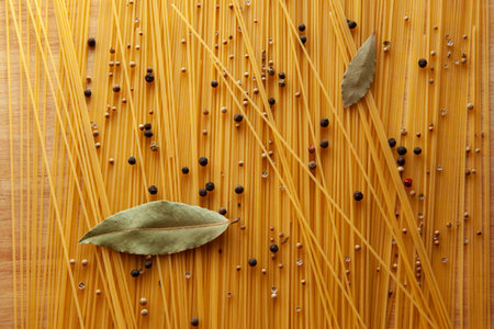 Artistic Spaghetti scattered on the table with bay leafs and black pepper peas. Italian food concept for publication, poster, screensaver, wallpaper, postcard, banner, cover, postの写真素材