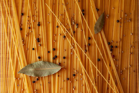 Food theme: raw pasta as whole background. Yellow Spaghetti scattered on the table with black pepper peas for publication, poster, calendar, post, screensaver, wallpaper, postcard, card, banner, coverの写真素材