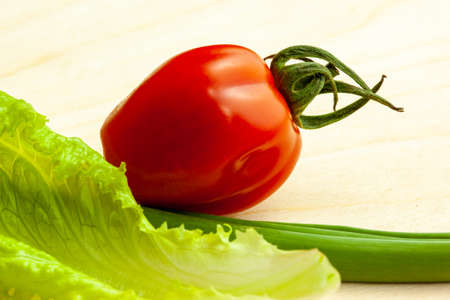 Still life from green onion and salad leaf and one tomato, close-up. Background with fresh vegetable for salad. Raw green and red vegetables for poster, calendar, card, banner, cover, websiteの写真素材