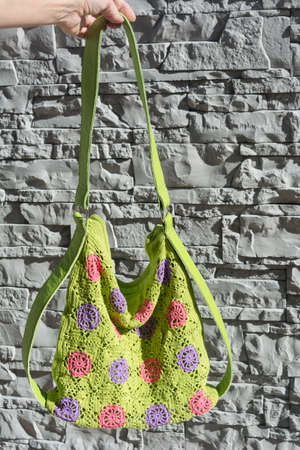 Colorful crocheted handbag behind the stone wall in the gardenの写真素材