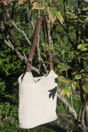 Cream crocheted handbag behind the bush in the garden in late summer on countrysideの写真素材
